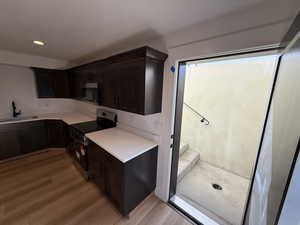 Kitchen featuring stainless steel appliances, light countertops, light wood-style flooring, a sink, and dark brown cabinetry