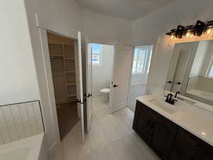 Full bathroom with a tub to relax in, toilet, vanity, a spacious closet, and tile patterned floors