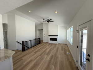 Unfurnished living room featuring vaulted ceiling, a fireplace, light wood-style flooring, and a textured ceiling