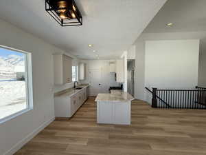 Kitchen featuring plenty of natural light, white cabinets, stove, light wood-type flooring, and a sink