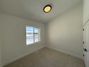 Spare room featuring light colored carpet, visible vents, lofted ceiling, and baseboards