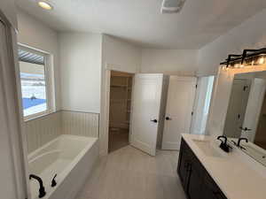 Bathroom with visible vents, a garden tub, a walk in closet, a textured ceiling, and vanity