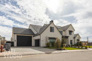 View of front of property featuring a garage, a chimney, a tiled roof, decorative driveway, and stucco siding