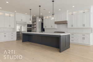 Kitchen with an island with sink, glass insert cabinets, built in appliances, light countertops, and white cabinetry