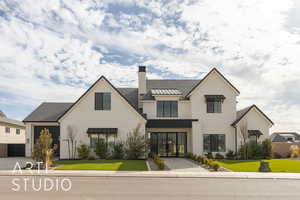 View of front of house with a standing seam roof, a chimney, a front lawn, and stucco siding