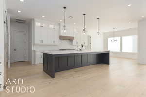 Kitchen featuring white cabinets, a large island, pendant lighting, and light countertops