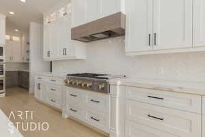 Kitchen featuring custom exhaust hood, glass insert cabinets, appliances with stainless steel finishes, white cabinetry, and light stone countertops