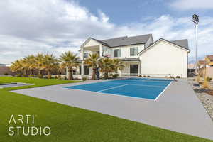 View of tennis court featuring basketball hoop, fence, and a yard