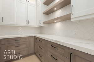 Kitchen with light stone counters, tasteful backsplash, white cabinetry, and open shelves