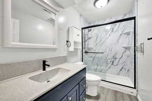 Full bath with toilet, vanity, wood finished floors, and a marble finish shower