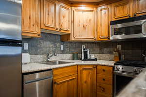 Kitchen with appliances with stainless steel finishes, brown cabinetry, a sink, and tasteful backsplash