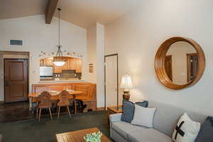 Living room with high vaulted ceiling, visible vents, dark colored carpet, and beam ceiling