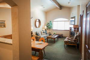 Carpeted living room with vaulted ceiling with beams and a textured wall