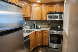 Kitchen with stainless steel appliances, brown cabinetry, backsplash, and light stone counters