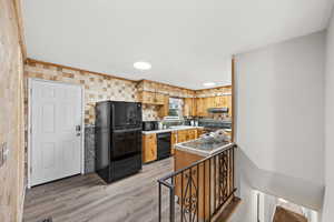 Kitchen featuring LVP flooring, under cabinet range hood, light countertops, and black appliances