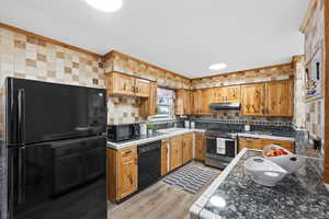 Kitchen featuring LVP flooring, under cabinet range hood, light countertops, and black appliances