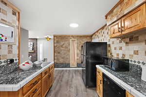 Kitchen featuring LVP flooring, under cabinet range hood, light countertops, and black appliances