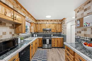 Kitchen featuring LVP flooring, under cabinet range hood, light countertops, and black appliances