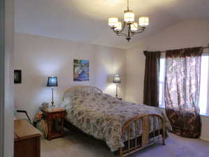 Bedroom with lofted ceiling, carpet flooring, and an inviting chandelier