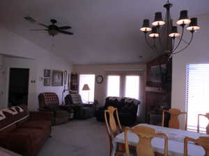 Dining space featuring ceiling fan with notable chandelier, vaulted ceiling, and light colored carpet