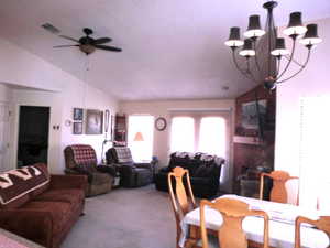 Dining area featuring lofted ceiling, light colored carpet, and ceiling fan with notable chandelier