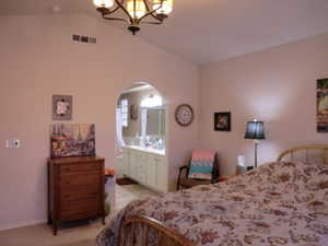 Bedroom featuring vaulted ceiling, ensuite bath, and a notable chandelier