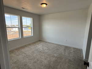 Spare room featuring carpet, visible vents, a textured ceiling, and baseboards