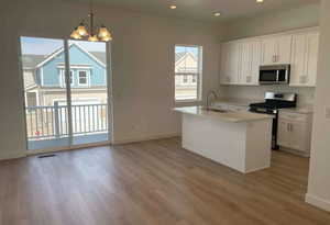 Kitchen with hanging light fixtures, white cabinetry, stainless steel appliances, and a sink