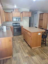 Kitchen with dark wood-style floors, stainless steel appliances, lofted ceiling, visible vents, and a kitchen island