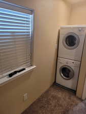 Clothes washing area featuring a textured wall, stacked washer and dryer, dark carpet, and laundry area