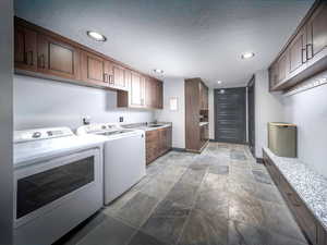 Laundry area and mud room, entry from garage, featuring a textured ceiling, washing machine and dryer, recessed lighting, cabinet space, and stone finish flooring