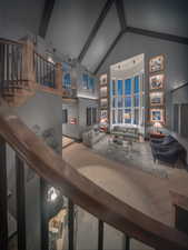 Dramatic living room featuring stairs, a high vaulted ceiling, a beamed ceiling, and abundant windows.