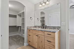 Bathroom with a walk in closet, vanity, and baseboards