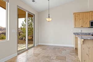 Kitchen featuring stainless steel microwave, decorative light fixtures, light countertops, stone tile flooring, and light brown cabinets