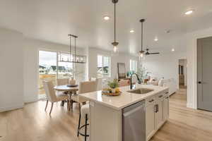 Kitchen featuring open floor plan, stainless steel dishwasher, a sink, and light wood-style flooring