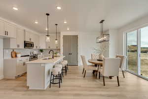 Kitchen with light wood-style flooring, a kitchen breakfast bar, a sink, light countertops, and appliances with stainless steel finishes