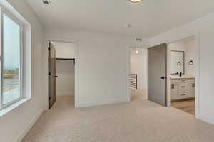 Unfurnished bedroom with light colored carpet, visible vents, ensuite bath, and baseboards