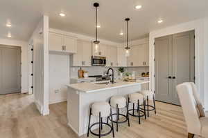 Kitchen with a sink, stainless steel microwave, light wood-style floors, light countertops, and a breakfast bar area