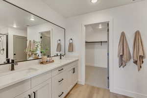 Full bathroom featuring a walk in closet, double vanity, wood finished floors, and a sink