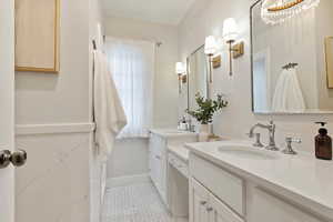 Primary bathroom double sinks, vanity, quartz countertops, marble flooring, and brass lighting