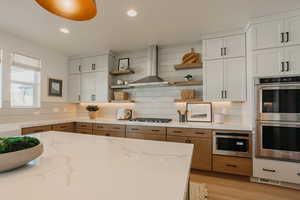 Kitchen with light stone countertops, wall chimney exhaust hood, white cabinetry, and open shelves