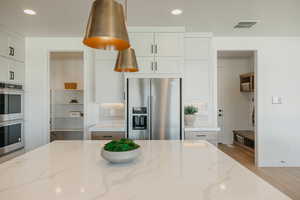 Kitchen featuring stainless steel appliances, visible vents, white cabinets, light wood-type flooring, and light stone countertops