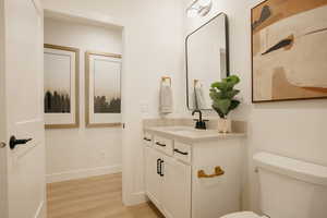 Half bathroom featuring toilet, wood finished floors, vanity, and baseboards