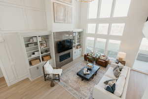 Living area featuring built in shelves, a decorative wall, a high ceiling, a tiled fireplace, and light wood-style floors