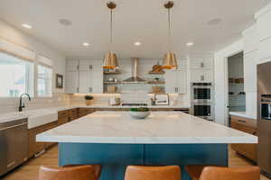 Kitchen with a sink, appliances with stainless steel finishes, wall chimney exhaust hood, open shelves, and decorative light fixtures