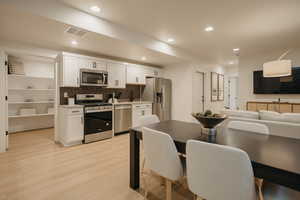 Kitchen featuring stainless steel appliances, recessed lighting, light countertops, light wood-style floors, and white cabinets