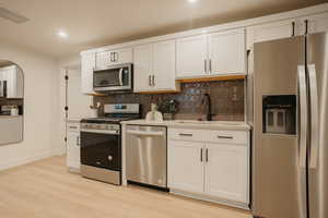 Kitchen with light countertops, visible vents, appliances with stainless steel finishes, white cabinetry, and a sink