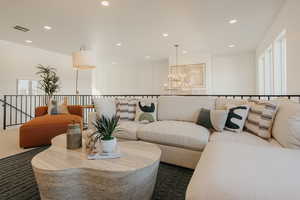 Carpeted living area featuring a notable chandelier, recessed lighting, visible vents, and a decorative wall