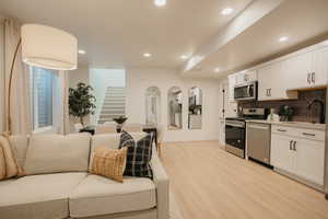 Kitchen featuring stainless steel appliances, light countertops, light wood-style floors, white cabinets, and a sink