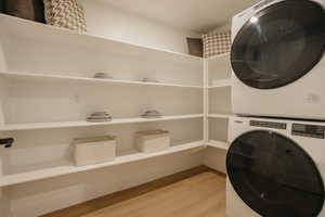 Clothes washing area featuring laundry area, stacked washing maching and dryer, and light wood finished floors